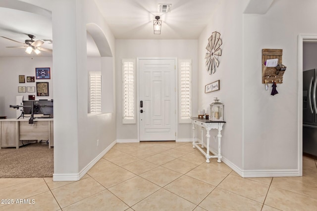 foyer with light tile patterned flooring, ceiling fan, baseboards, and arched walkways