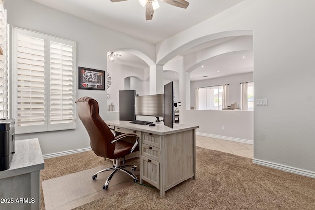 home office featuring light carpet, a ceiling fan, arched walkways, and baseboards
