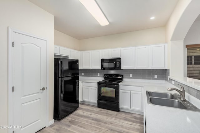 kitchen featuring black appliances, light wood-style flooring, a sink, backsplash, and white cabinets