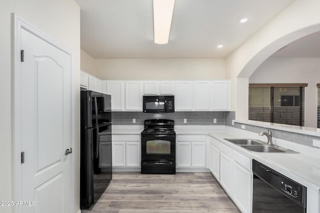 kitchen featuring light wood finished floors, backsplash, white cabinets, black appliances, and a sink