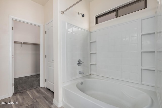 bathroom with a walk in closet, wood finished floors, baseboards, and shower / bathtub combination