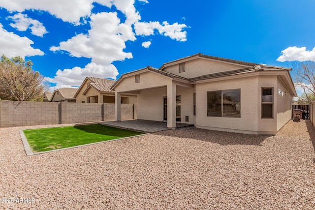 rear view of property featuring a tiled roof, stucco siding, a fenced backyard, and a patio area