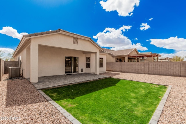 back of house with central AC, stucco siding, a lawn, a fenced backyard, and a patio