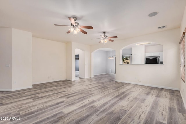 unfurnished living room featuring light wood-type flooring, visible vents, arched walkways, and baseboards