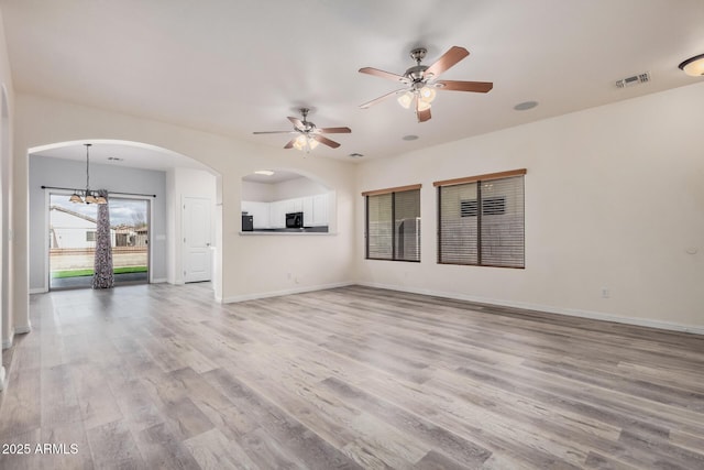 unfurnished living room featuring wood finished floors, baseboards, visible vents, arched walkways, and ceiling fan with notable chandelier