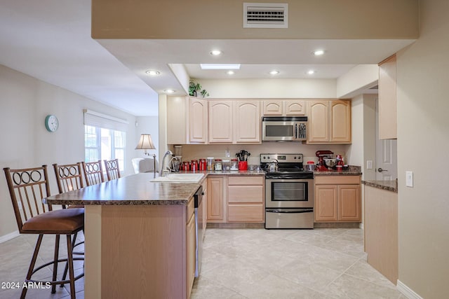 kitchen with light brown cabinets, sink, a breakfast bar area, kitchen peninsula, and stainless steel appliances