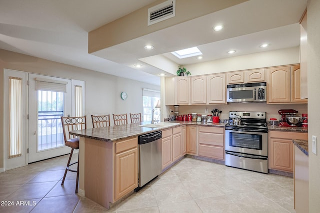 kitchen featuring sink, kitchen peninsula, a kitchen bar, light brown cabinetry, and appliances with stainless steel finishes