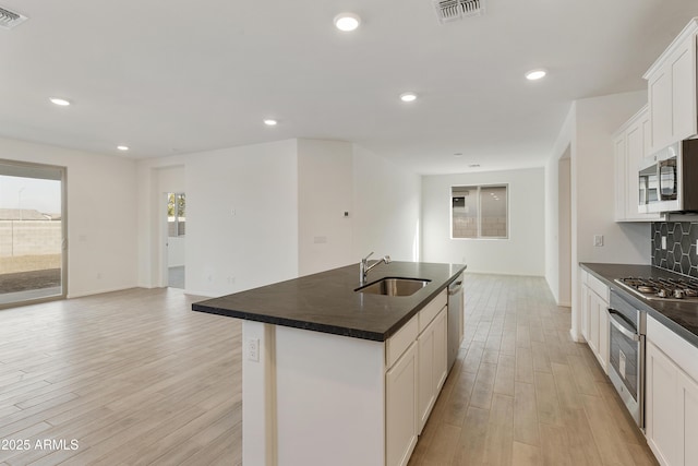 kitchen with a center island with sink, white cabinets, sink, appliances with stainless steel finishes, and light hardwood / wood-style floors