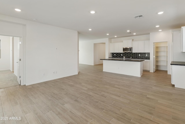 kitchen featuring sink, a kitchen island with sink, light hardwood / wood-style flooring, decorative backsplash, and white cabinets