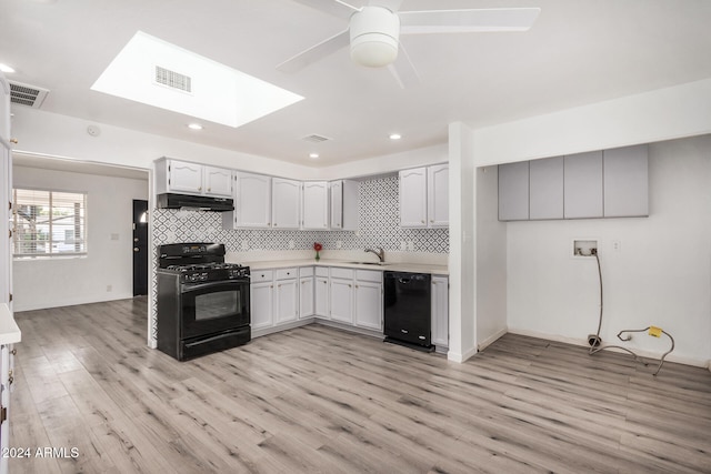 kitchen featuring decorative backsplash, a skylight, sink, black appliances, and light hardwood / wood-style floors