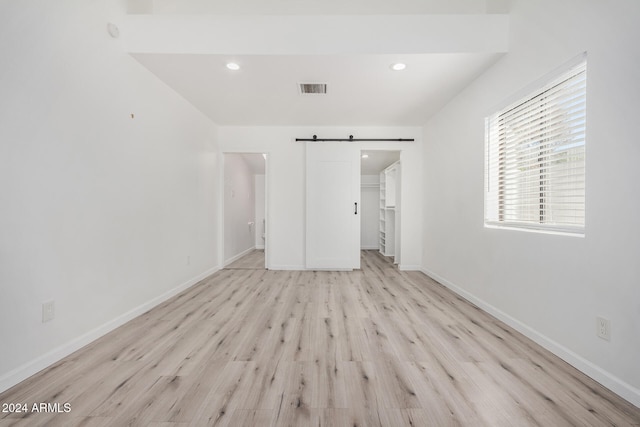 unfurnished bedroom with a spacious closet, a barn door, light wood-type flooring, and a closet