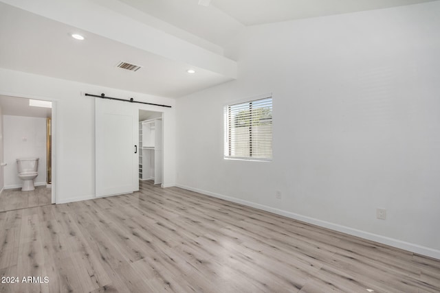 unfurnished bedroom with a barn door, light hardwood / wood-style floors, connected bathroom, and a closet