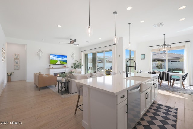 kitchen with sink, white cabinetry, decorative light fixtures, stainless steel dishwasher, and a kitchen island with sink