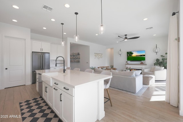 kitchen with pendant lighting, a breakfast bar area, white cabinets, high end refrigerator, and a kitchen island with sink