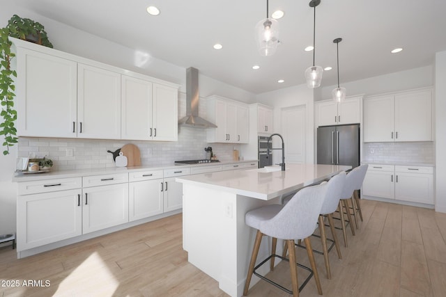 kitchen with white cabinetry, wall chimney range hood, a kitchen island with sink, and stainless steel appliances