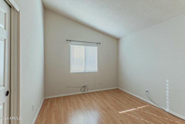 spare room with hardwood / wood-style floors, lofted ceiling, and a textured ceiling