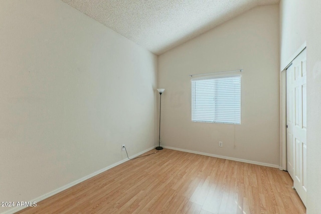 empty room with a textured ceiling, light wood-type flooring, and lofted ceiling