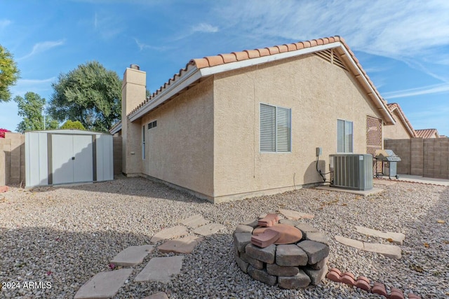 back of property featuring cooling unit, a storage unit, and an outdoor fire pit