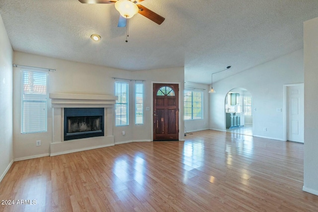 unfurnished living room with a textured ceiling, light hardwood / wood-style floors, and lofted ceiling