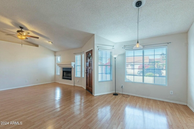 unfurnished living room with a textured ceiling, ceiling fan, light hardwood / wood-style floors, and vaulted ceiling