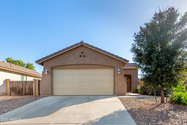 view of front facade with a tiled roof, a garage, fence, concrete driveway, and stucco siding
