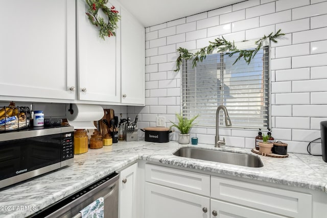 kitchen featuring light stone countertops, appliances with stainless steel finishes, tasteful backsplash, sink, and white cabinetry