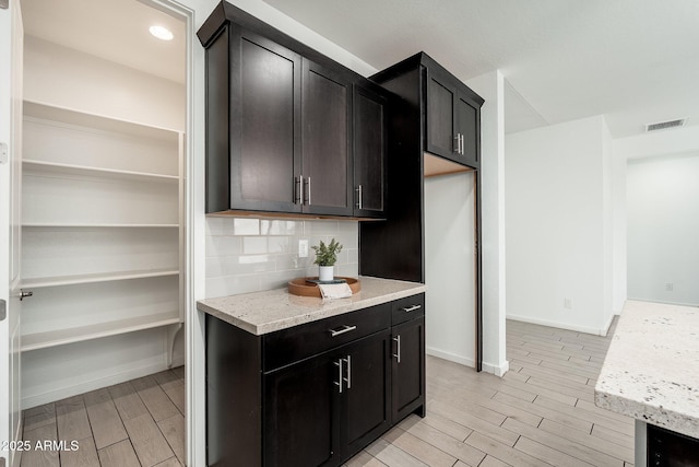 17652 W Fetlock Trl, Surprise, AZ 85387 - kitchen with wood finish floors, backsplash, light stone countertops, and dark cabinetry