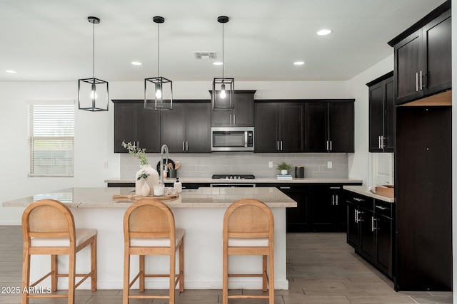 17652 W Fetlock Trl, Surprise, AZ 85387 - kitchen with stainless steel microwave, light wood finished floors, decorative backsplash, a kitchen island with sink, and dark cabinets