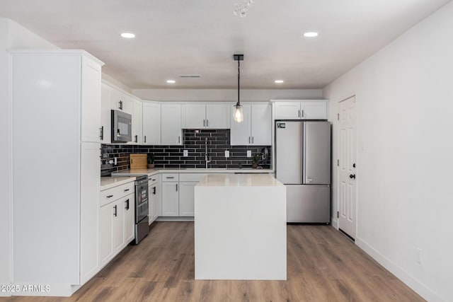 kitchen featuring black range with electric cooktop, a kitchen island, pendant lighting, white cabinets, and stainless steel refrigerator