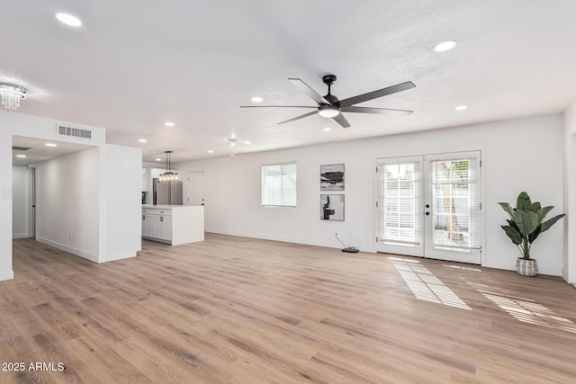 unfurnished living room with french doors, ceiling fan with notable chandelier, and light wood-type flooring