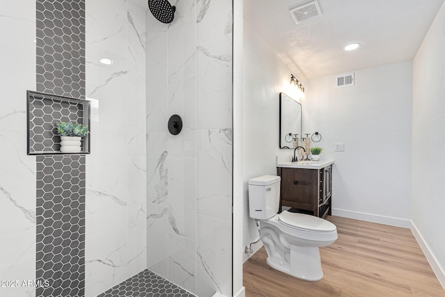 bathroom with a tile shower, vanity, wood-type flooring, and toilet