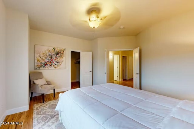 bedroom with a spacious closet, wood-type flooring, a closet, and ceiling fan