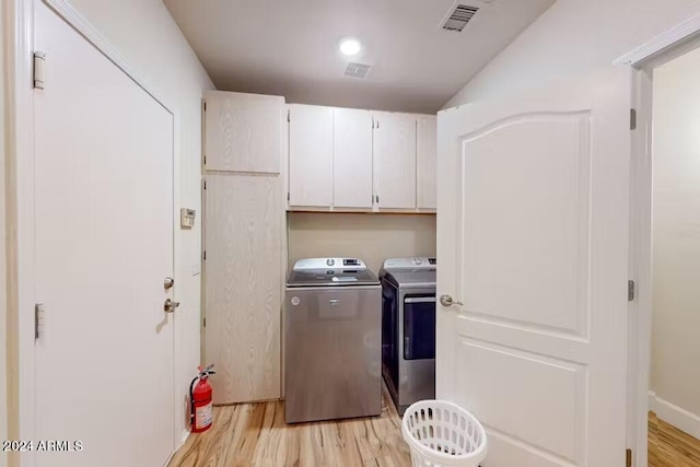 clothes washing area featuring cabinets, light hardwood / wood-style flooring, and washer and clothes dryer