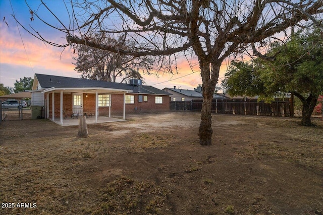 back house at dusk featuring a patio area and a lawn