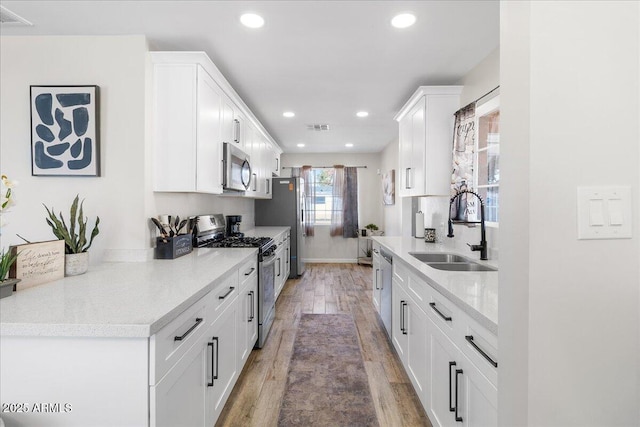 kitchen with light wood-type flooring, stainless steel appliances, sink, and white cabinets