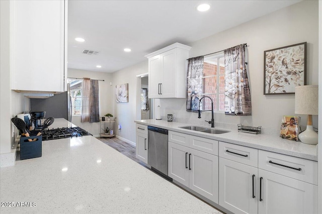 kitchen with sink, white cabinets, stainless steel dishwasher, light stone countertops, and light wood-type flooring