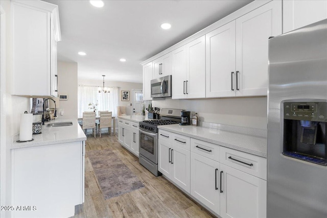 kitchen featuring pendant lighting, white cabinetry, sink, light hardwood / wood-style floors, and stainless steel appliances