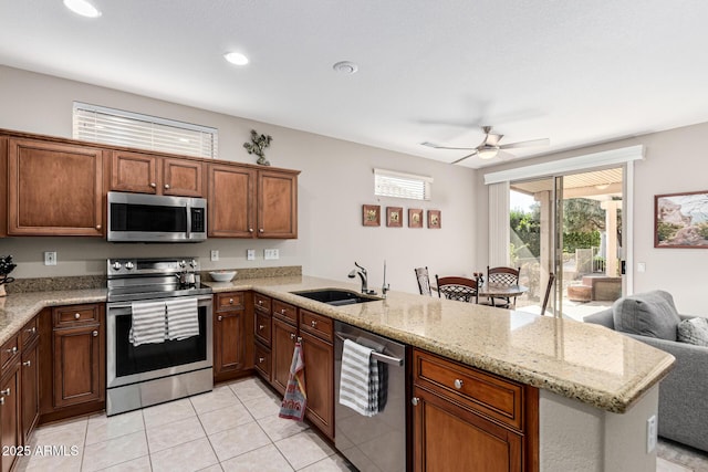 kitchen featuring stainless steel appliances, sink, light stone counters, and kitchen peninsula