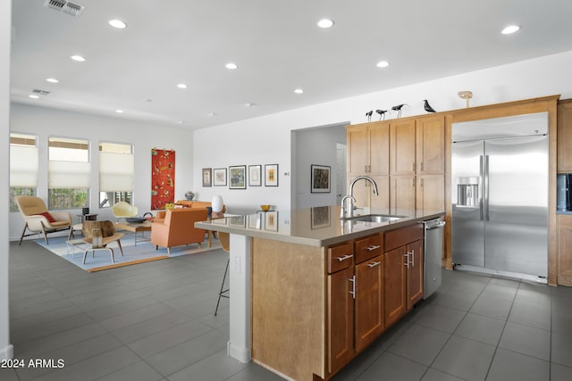 kitchen featuring dark tile patterned flooring, a center island with sink, a kitchen bar, sink, and appliances with stainless steel finishes