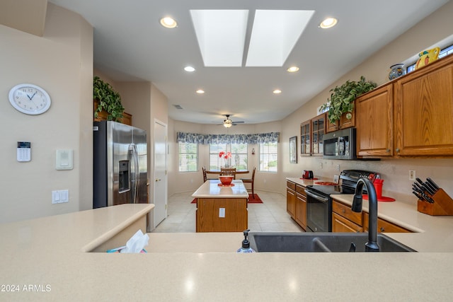 kitchen with a skylight, ceiling fan, stainless steel appliances, a kitchen island, and light tile patterned flooring