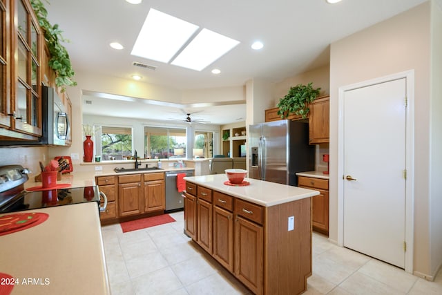 kitchen with a center island, sink, a skylight, ceiling fan, and appliances with stainless steel finishes