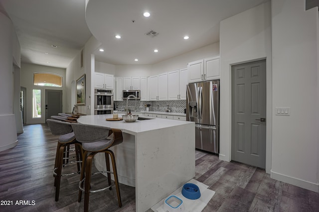 kitchen with appliances with stainless steel finishes, a kitchen breakfast bar, white cabinets, dark hardwood / wood-style flooring, and an island with sink