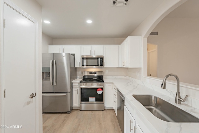 kitchen featuring white cabinets, appliances with stainless steel finishes, light stone counters, and sink