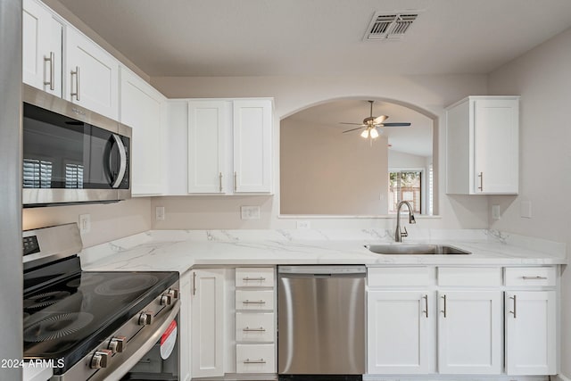 kitchen featuring ceiling fan, sink, light stone counters, white cabinets, and appliances with stainless steel finishes