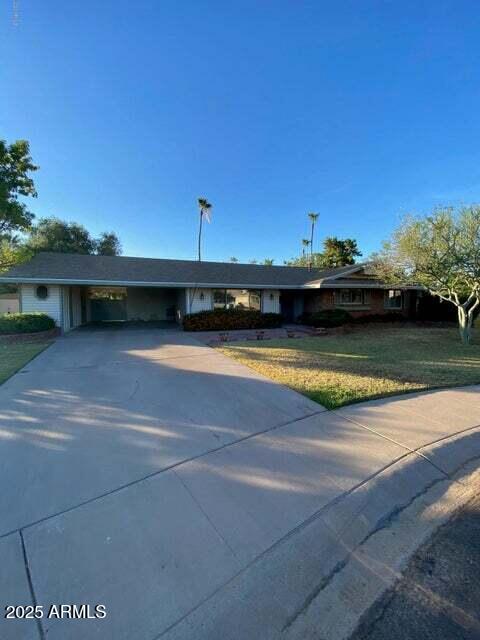 ranch-style home featuring concrete driveway, a front yard, and an attached carport