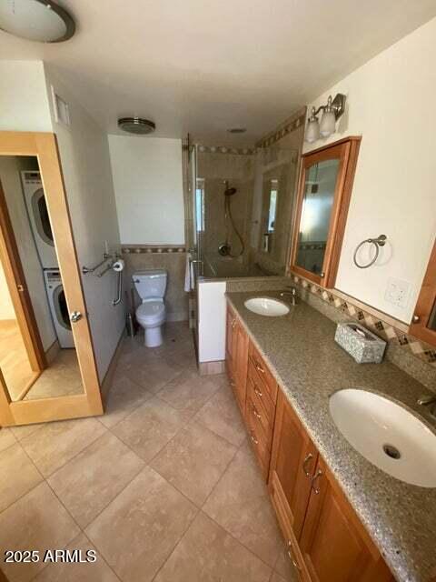 bathroom with stacked washer / drying machine, a shower stall, double vanity, tile patterned flooring, and tile walls