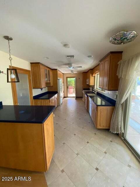 kitchen featuring dark countertops, ceiling fan, brown cabinets, and freestanding refrigerator