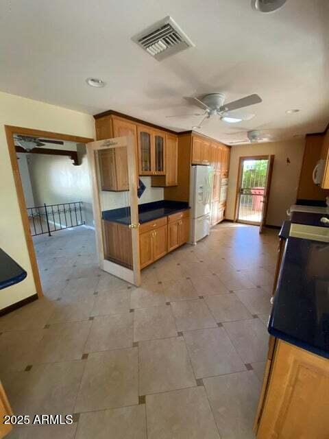 kitchen featuring white refrigerator with ice dispenser, ceiling fan, brown cabinetry, glass insert cabinets, and dark countertops