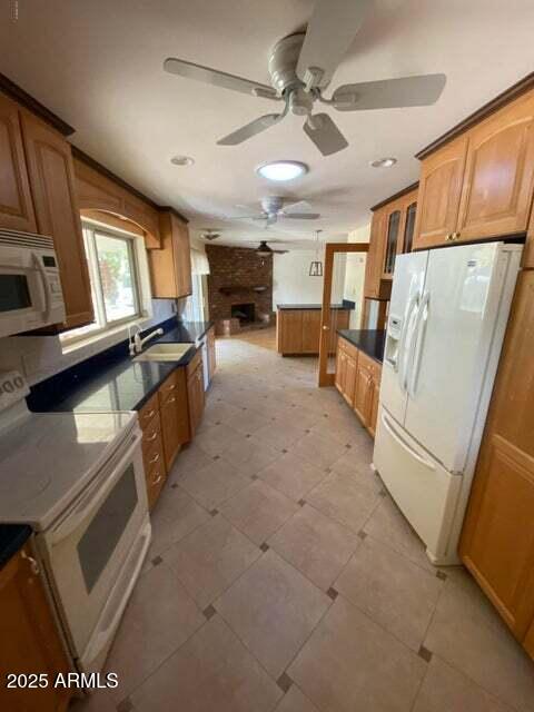 kitchen featuring white appliances, ceiling fan, a sink, a large fireplace, and recessed lighting
