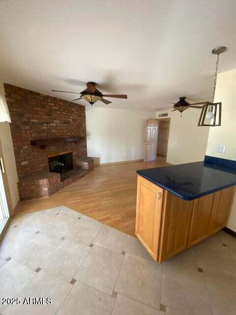 kitchen with ceiling fan, light tile patterned floors, dark countertops, and a fireplace